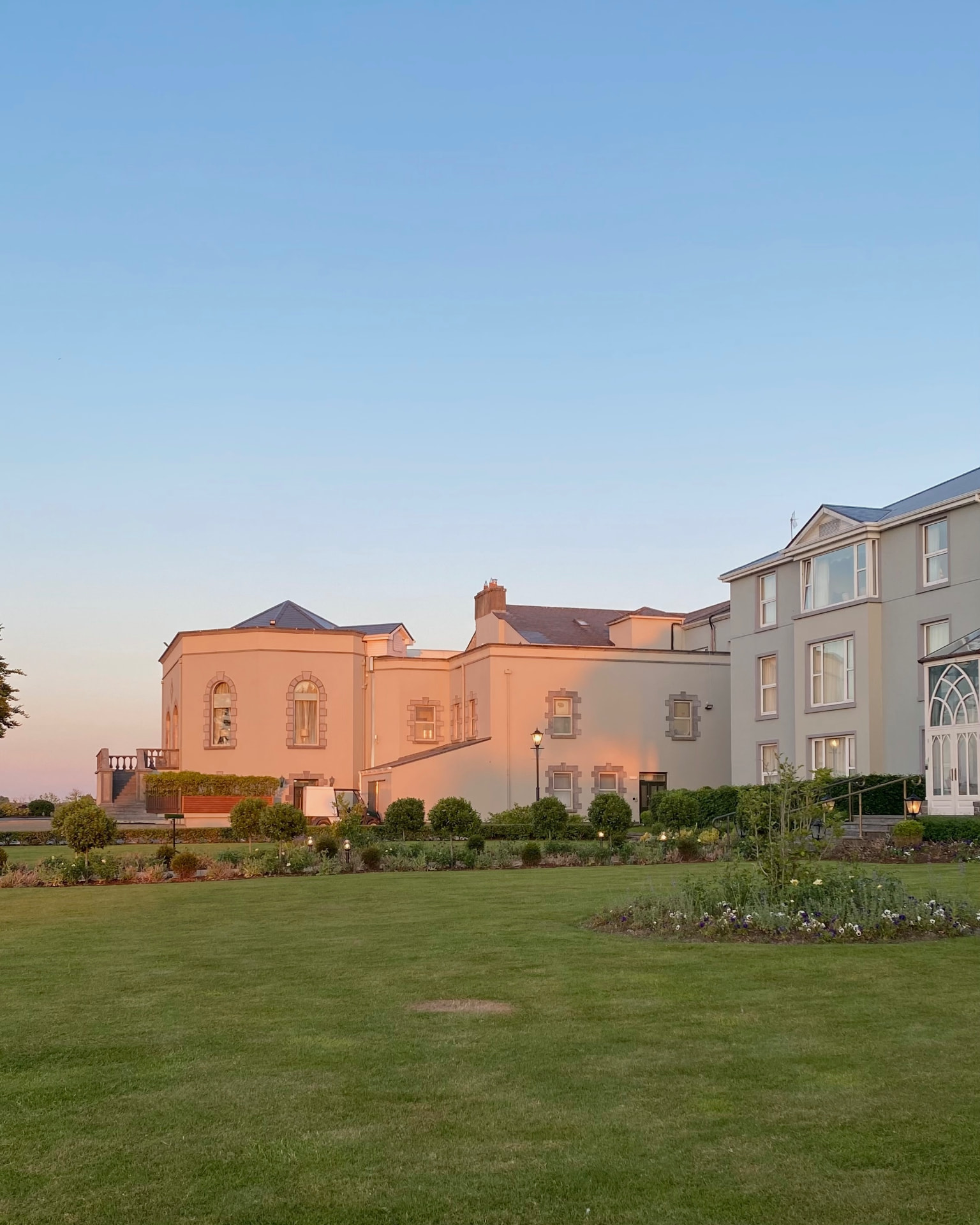 Historic estate venue glowing at golden hour beyond manicured lawns