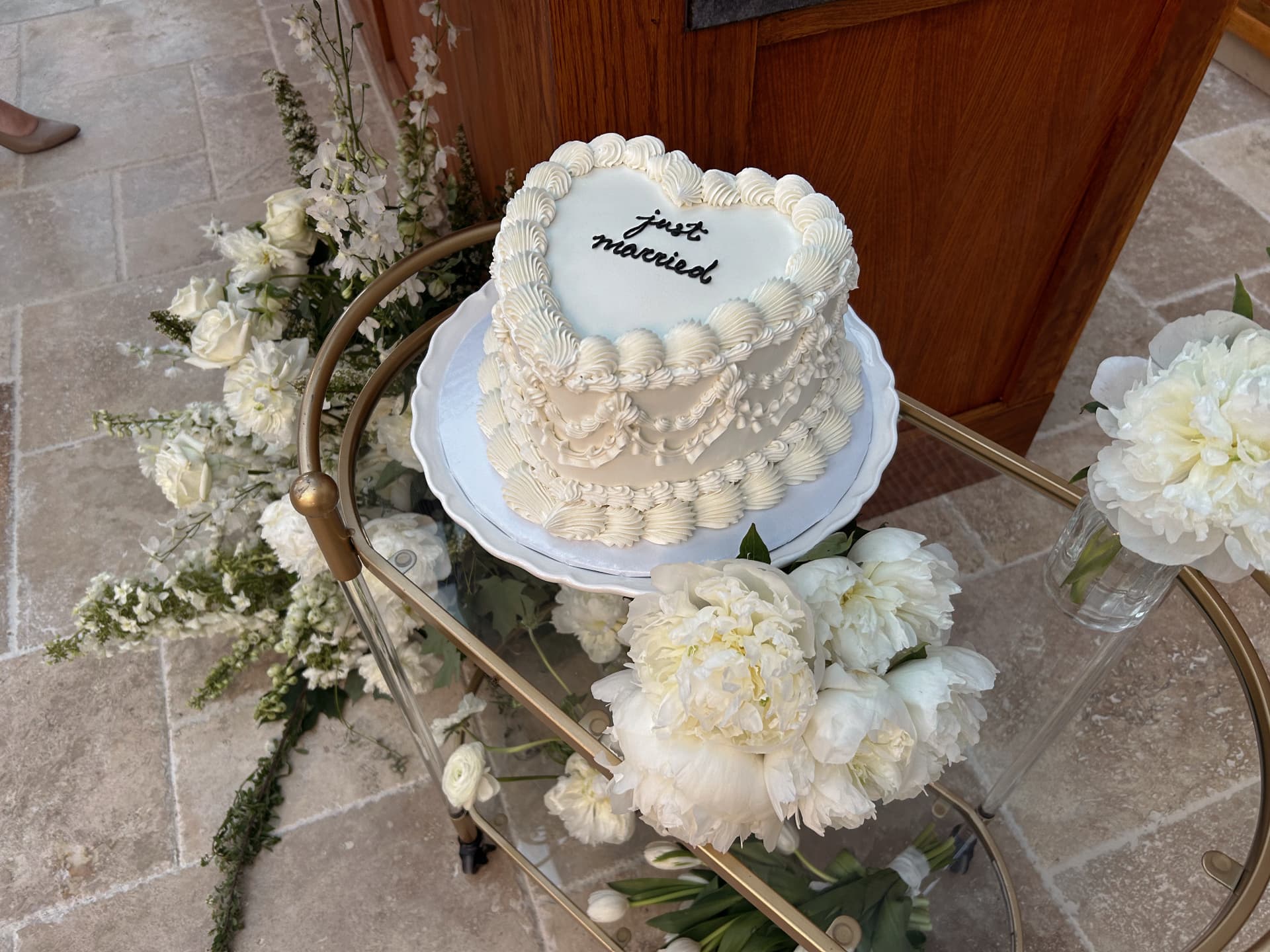 Heart-shaped just married cake on a gold bar cart with peonies
