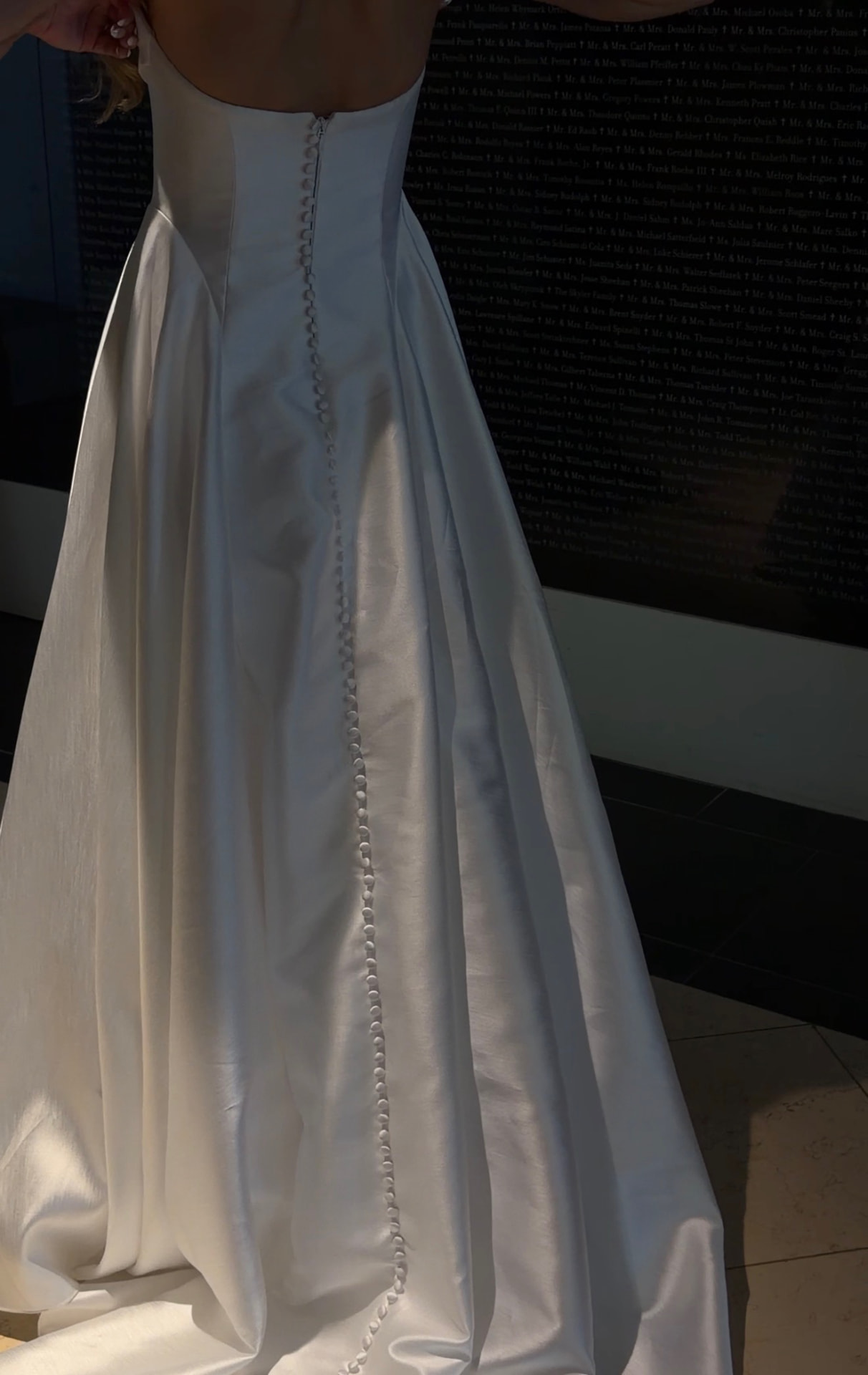 Back of a satin bridal gown with a long row of covered buttons and full train