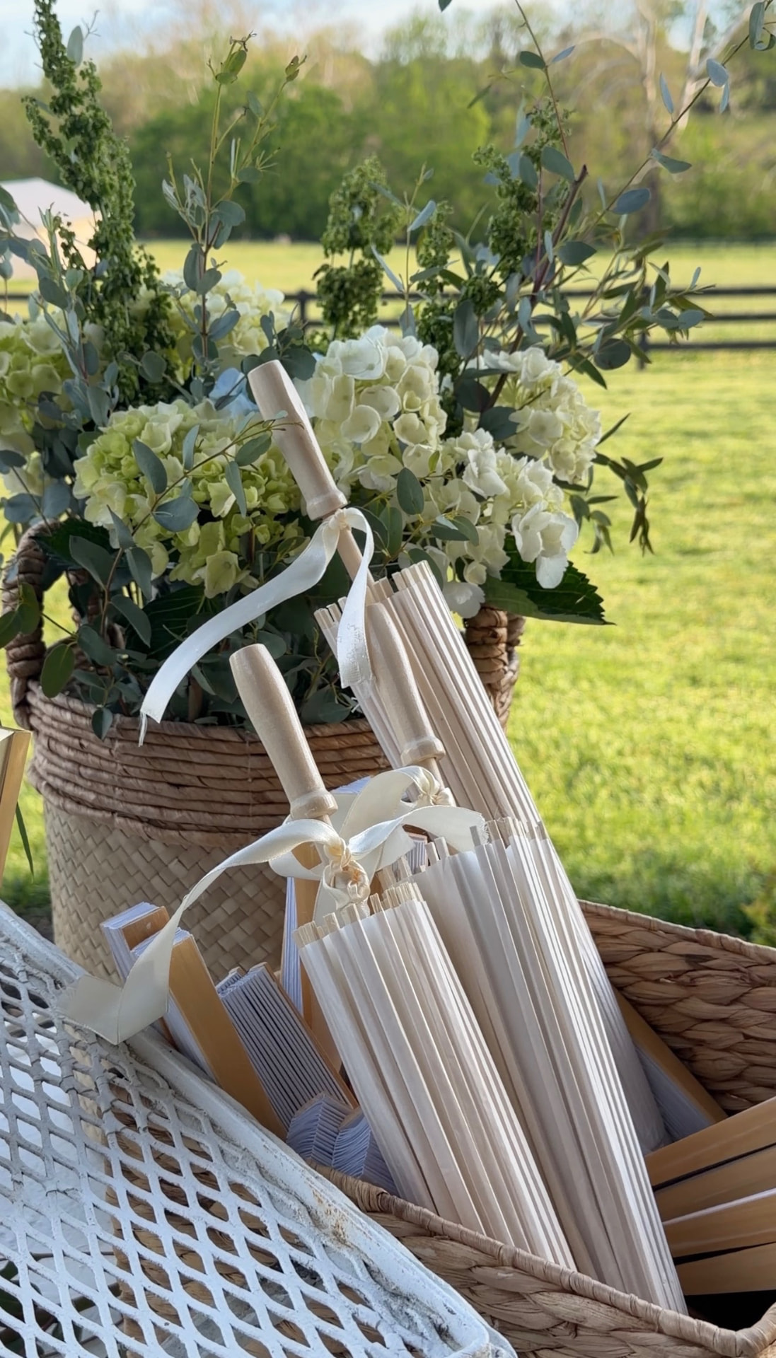 Ivory parasols and programs in a woven basket beside white hydrangeas