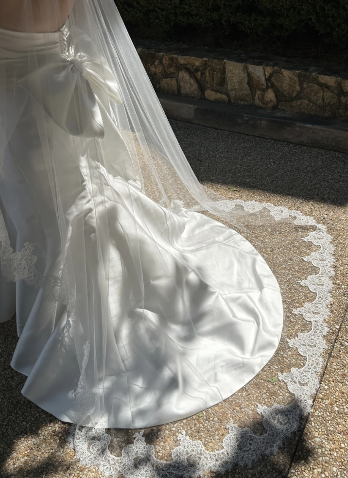 Lace-edged cathedral veil trailing over a satin gown train in the sunlight