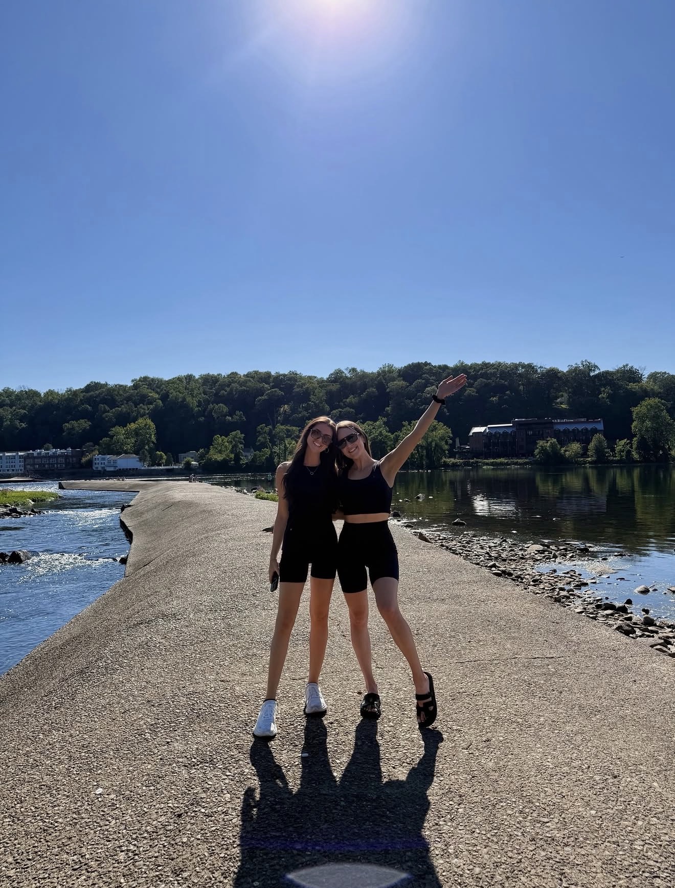 Two friends waving on a riverside path in the sunshine