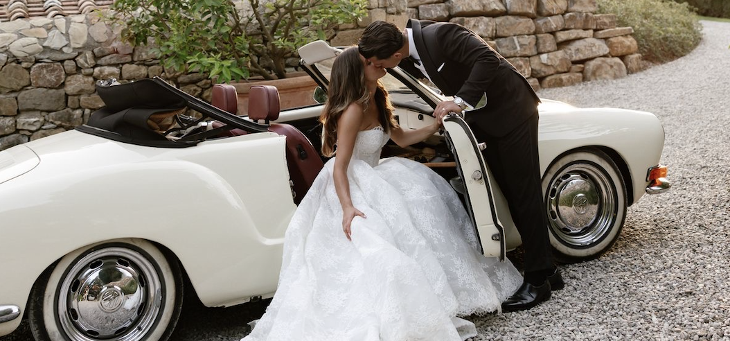 Bride and groom kissing beside a vintage white convertible