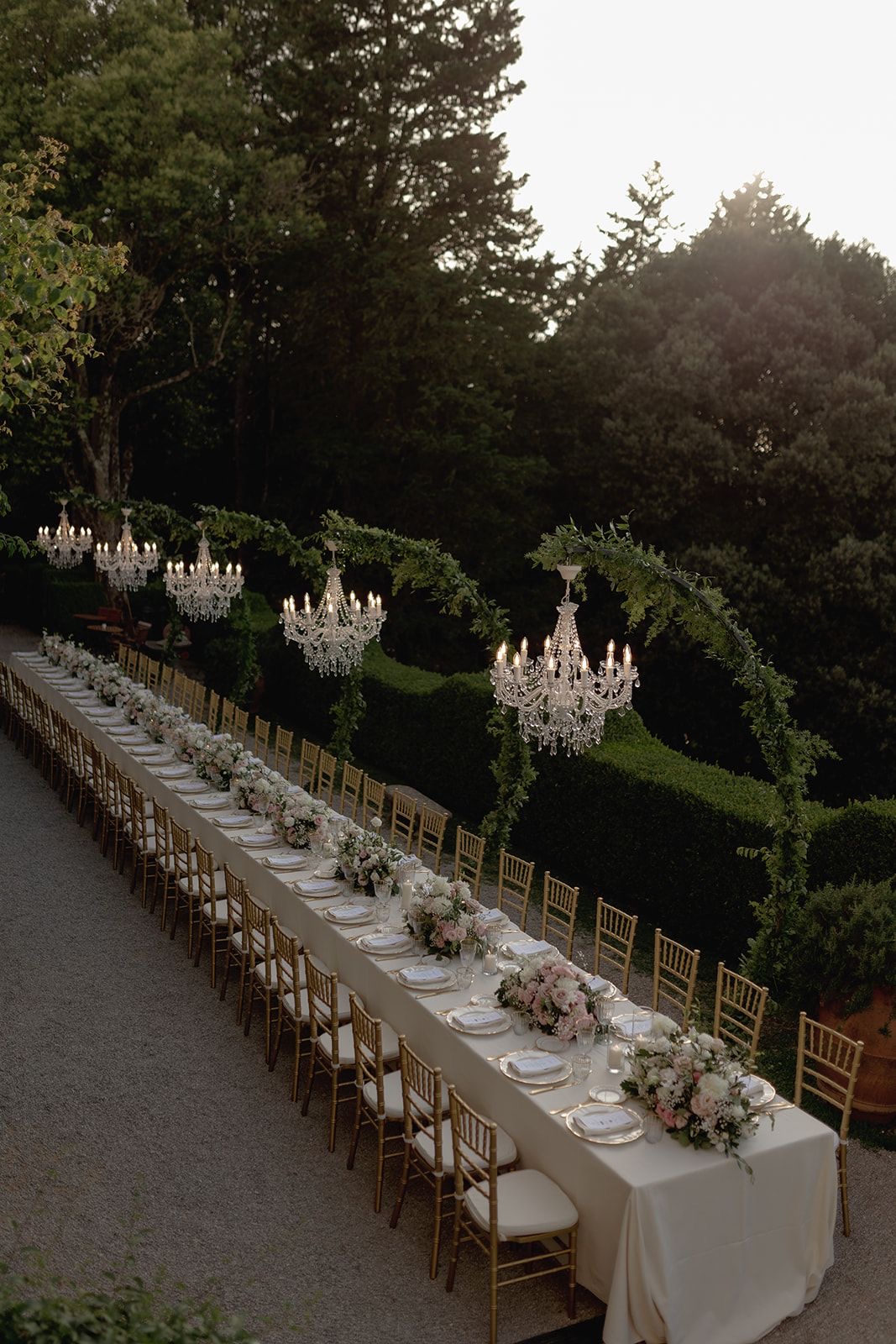 Long garden reception table beneath crystal chandeliers at dusk